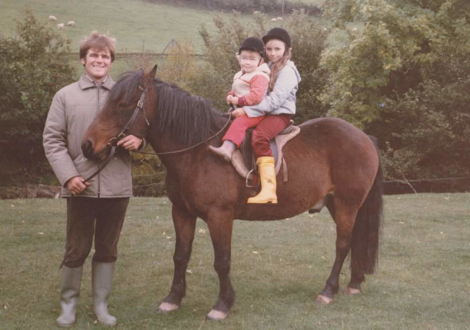 Jess and Sophie as children sitting on pony with Father Mike